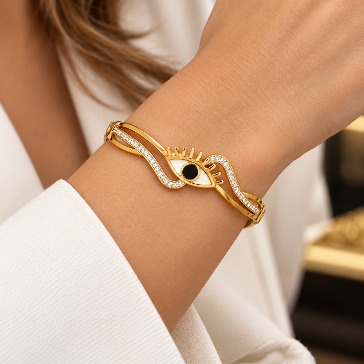 Noura goudkleurige oog armband gedragen om de pols bij een witte mouw